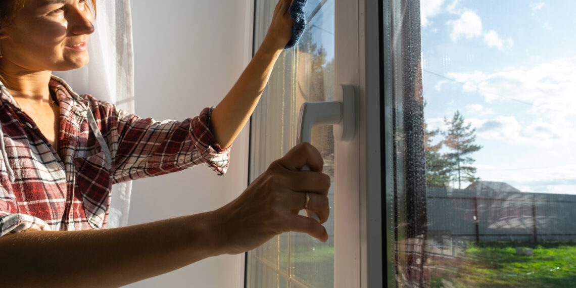 Close-up of a person opening a stuck wooden window frame, showing signs of swelling and friction along the edges.