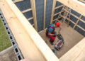 Person assembling a wooden garden shed frame with tools during shed installation in a UK garden
