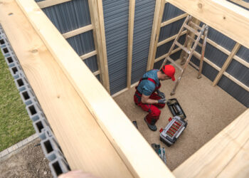 Person assembling a wooden garden shed frame with tools during shed installation in a UK garden