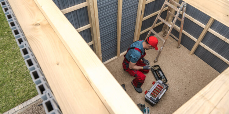 Person assembling a wooden garden shed frame with tools during shed installation in a UK garden