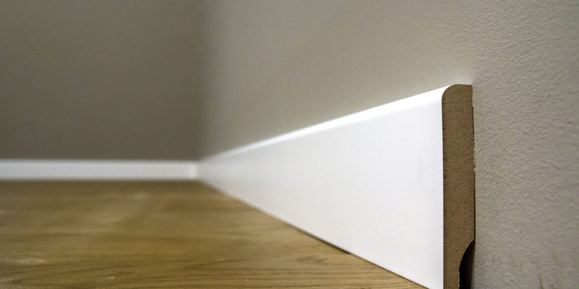 Close-up of damaged skirting board with visible chips and dents being repaired using wood filler and a putty knife.