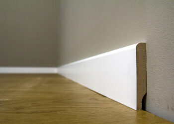 Close-up of damaged skirting board with visible chips and dents being repaired using wood filler and a putty knife.