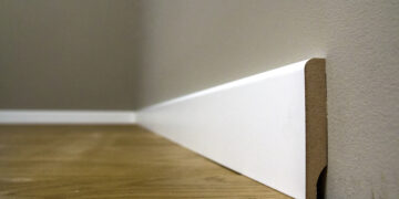 Close-up of damaged skirting board with visible chips and dents being repaired using wood filler and a putty knife.