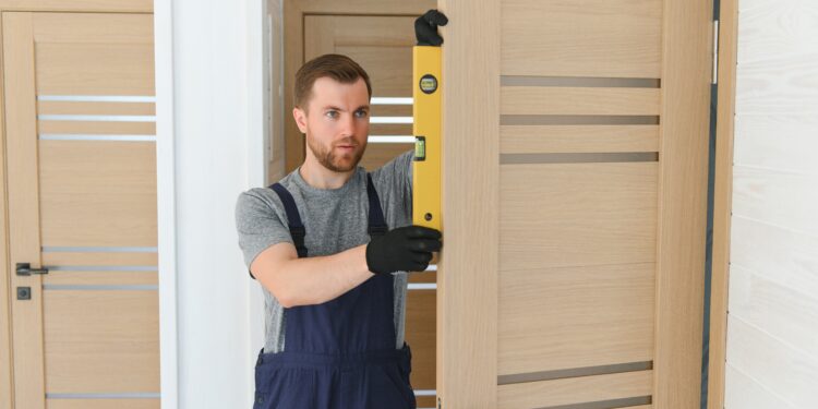 Close-up of a misaligned interior door scraping against the frame, with visible uneven gaps and a hand adjusting the hinge with a screwdriver.