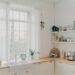 Bright budget-friendly kitchen with white cabinets, rustic wooden worktops, open shelving, and natural light streaming through large windows.
