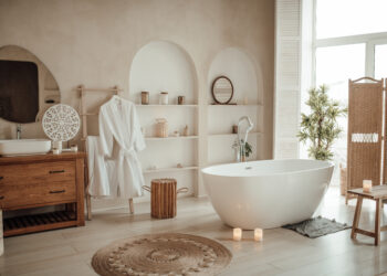 Elegant modern bathroom featuring a freestanding bathtub, wooden vanity unit, soft neutral décor, and natural light streaming through large windows.