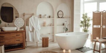 Elegant modern bathroom featuring a freestanding bathtub, wooden vanity unit, soft neutral décor, and natural light streaming through large windows.