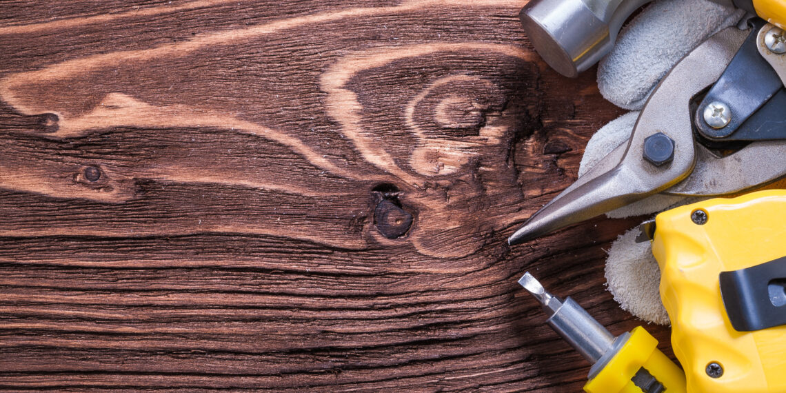 A handyman using a drill to assemble wooden furniture in a modern living room while unpacked boxes and tools are spread across the floor.