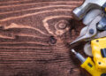 A handyman using a drill to assemble wooden furniture in a modern living room while unpacked boxes and tools are spread across the floor.