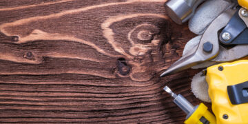 A handyman using a drill to assemble wooden furniture in a modern living room while unpacked boxes and tools are spread across the floor.