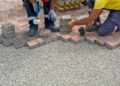 Workers installing a block paving driveway by carefully laying brick pavers over a gravel base outdoors
