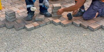 Workers installing a block paving driveway by carefully laying brick pavers over a gravel base outdoors