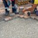 Workers installing a block paving driveway by carefully laying brick pavers over a gravel base outdoors