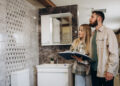 Couple reviewing bathroom renovation options in a showroom with modern wall tiles, vanity unit, and contemporary bathroom fittings.