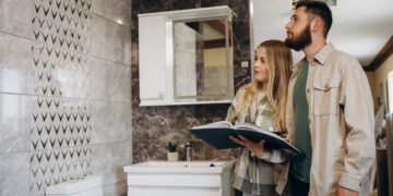 Couple reviewing bathroom renovation options in a showroom with modern wall tiles, vanity unit, and contemporary bathroom fittings.