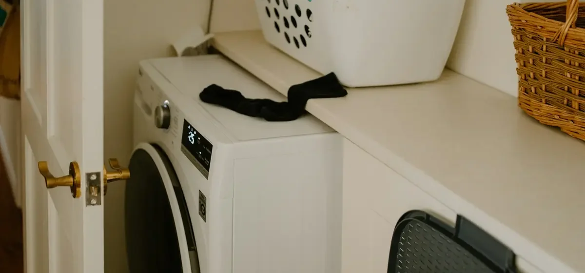 White washing machine beside a laundry basket and stray sock