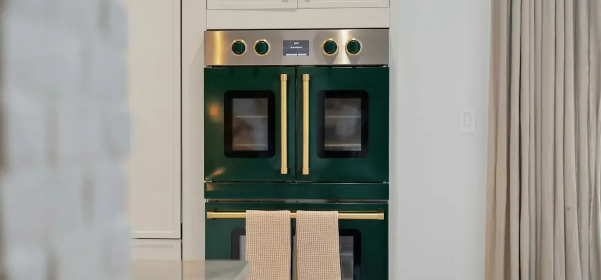 Dark green double oven with brass handles and hanging towels