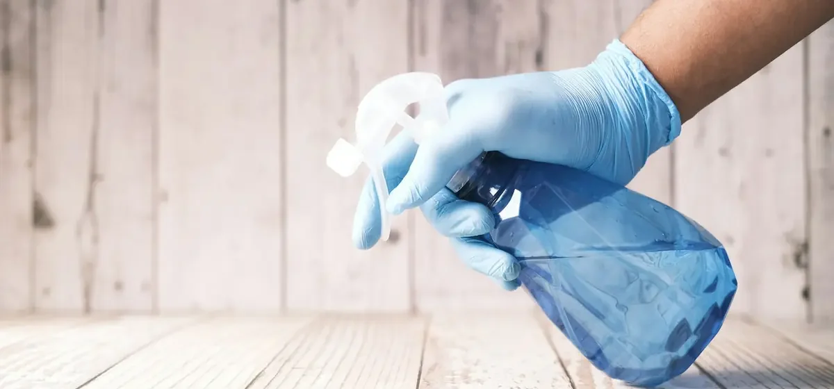 Gloved hand holding a blue spray cleaning bottle