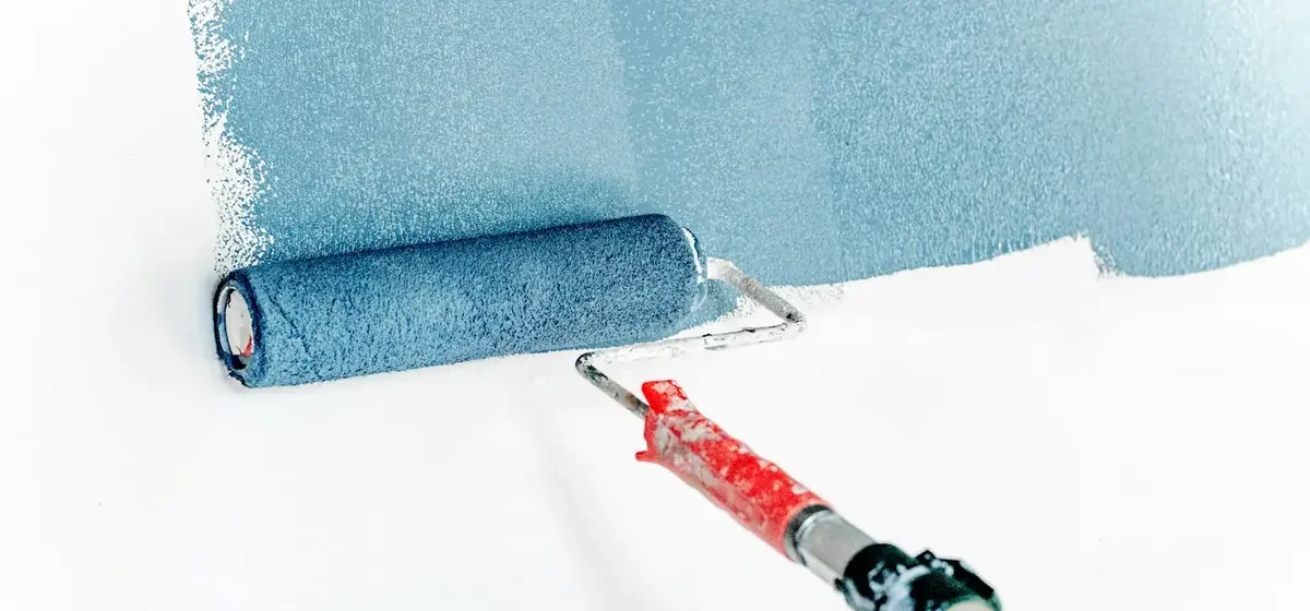 Paint roller spreading blue paint across a white wall