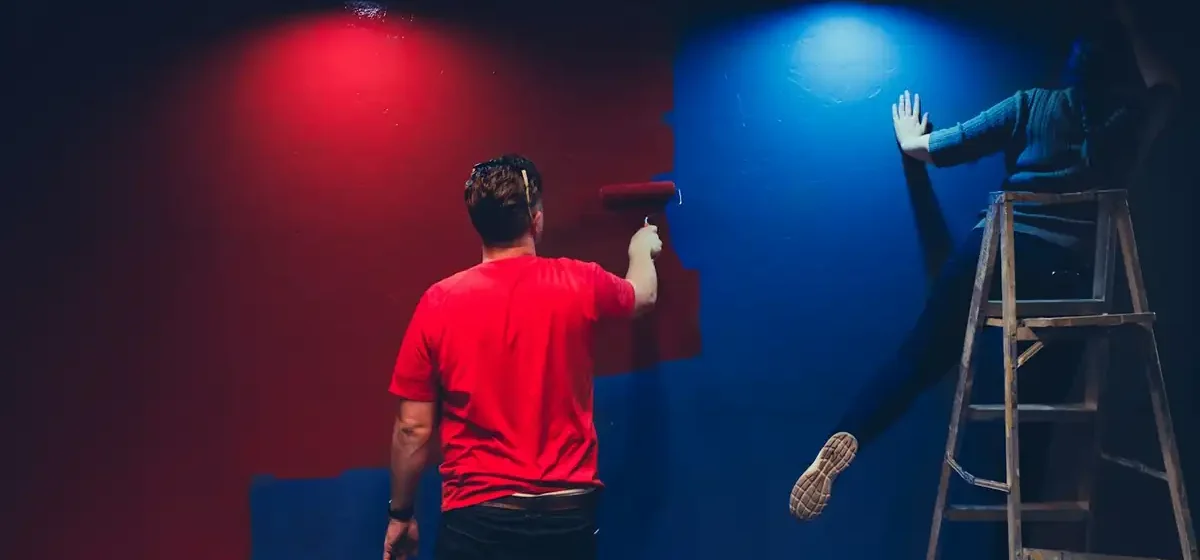 Two people painting an interior wall with rollers