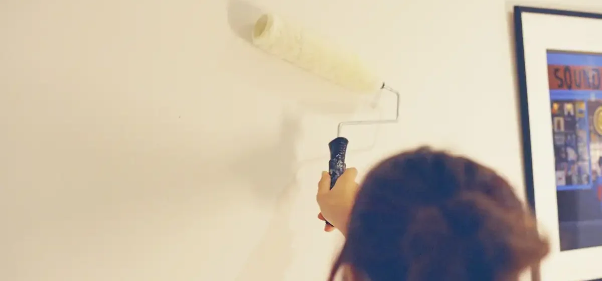 Person rolling pale paint onto a wall indoors