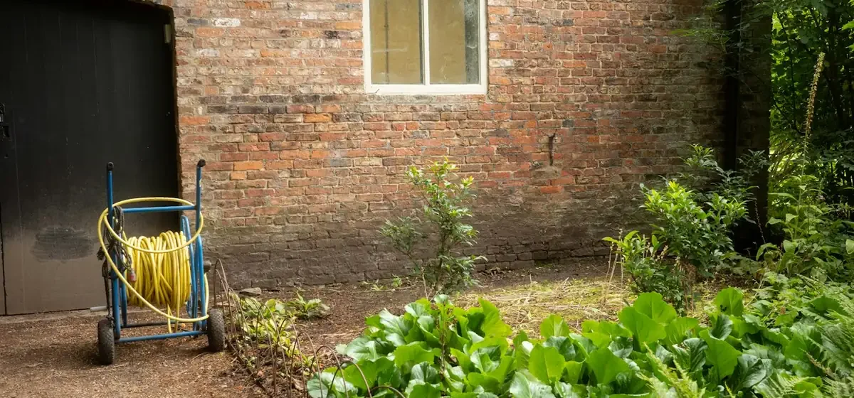 Yellow hose on a cart beside a brick outbuilding