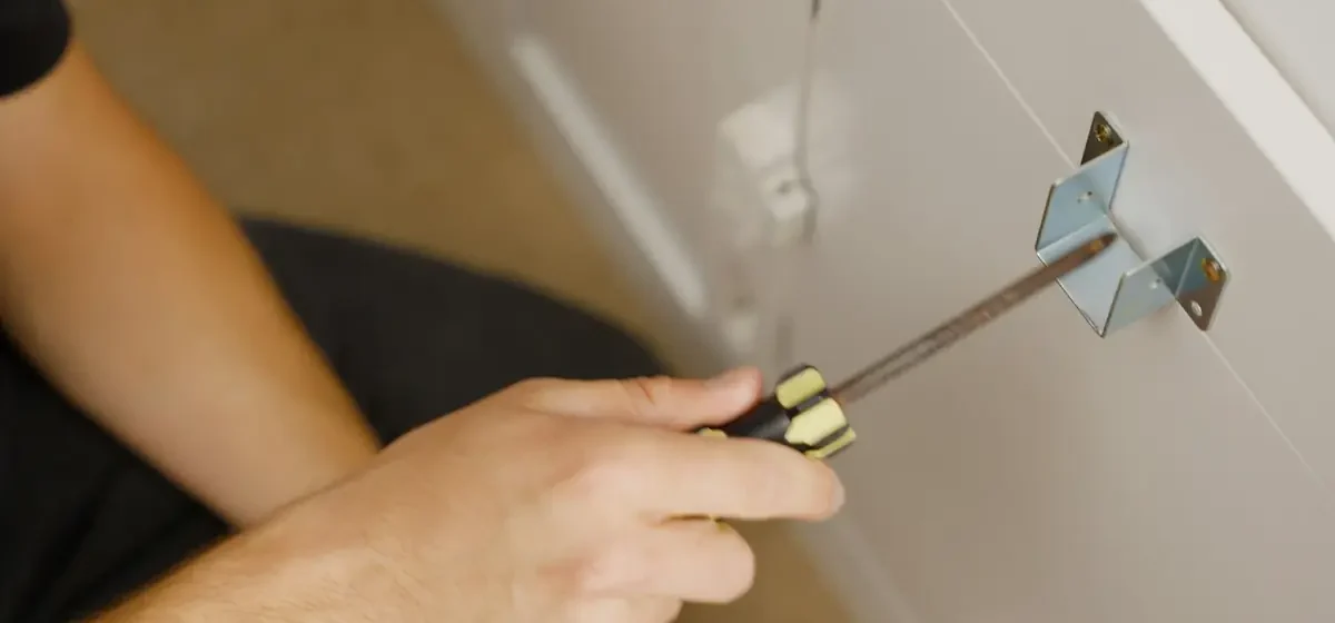 Hands screwing a metal bracket onto flat-pack furniture