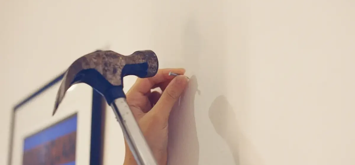 Hand holding a nail against a wall with hammer raised