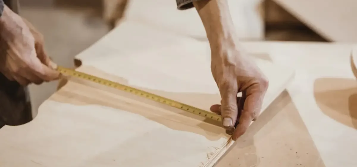 Person measuring a length of timber board with a tape measure
