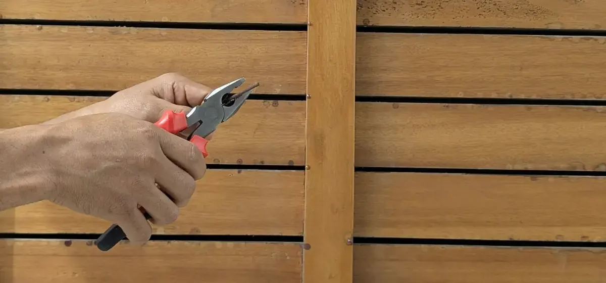 Hands using pliers on a screw against a wooden fence