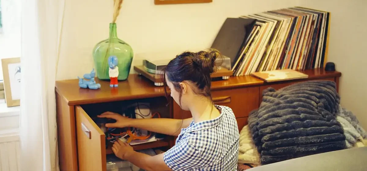 Woman kneeling to sort cables inside a wooden cabinet