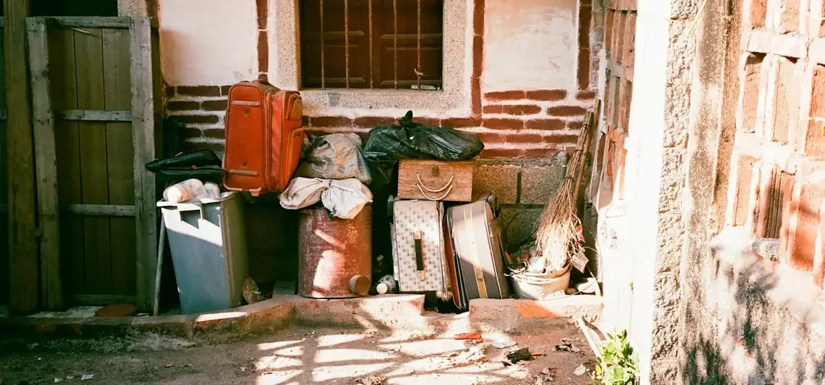 Stacked suitcases and discarded belongings against a brick wall