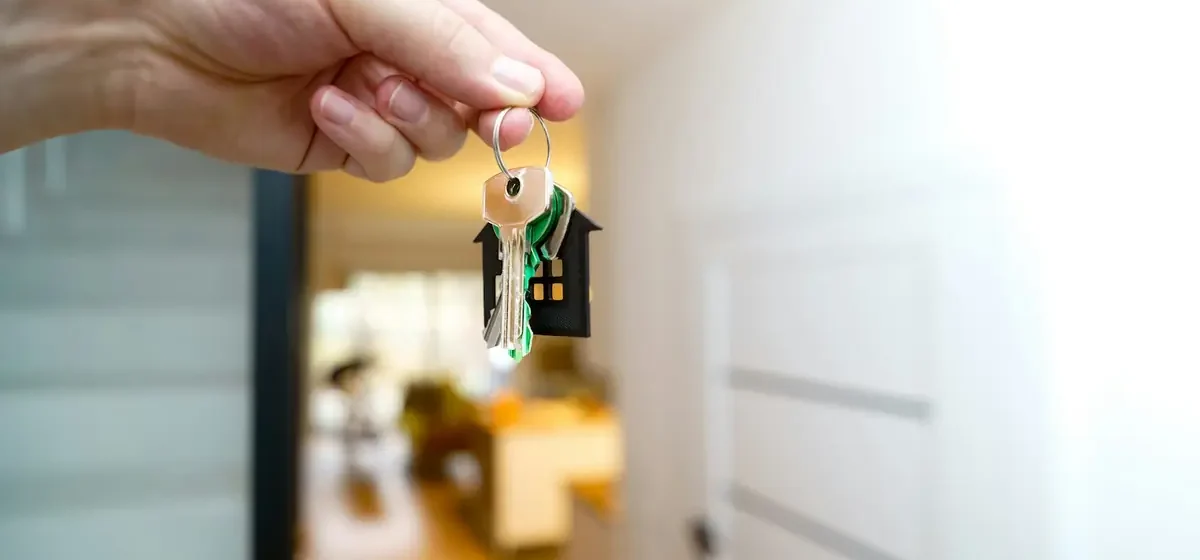 Hand holding house keys in front of an entrance hallway