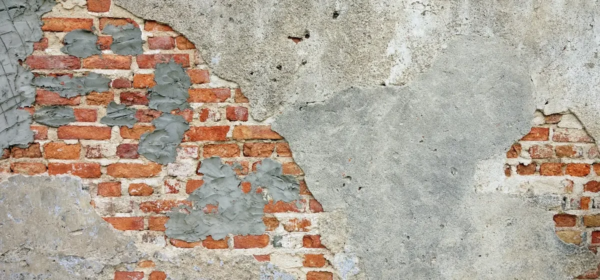 Weathered brick wall with patches of crumbling grey plaster