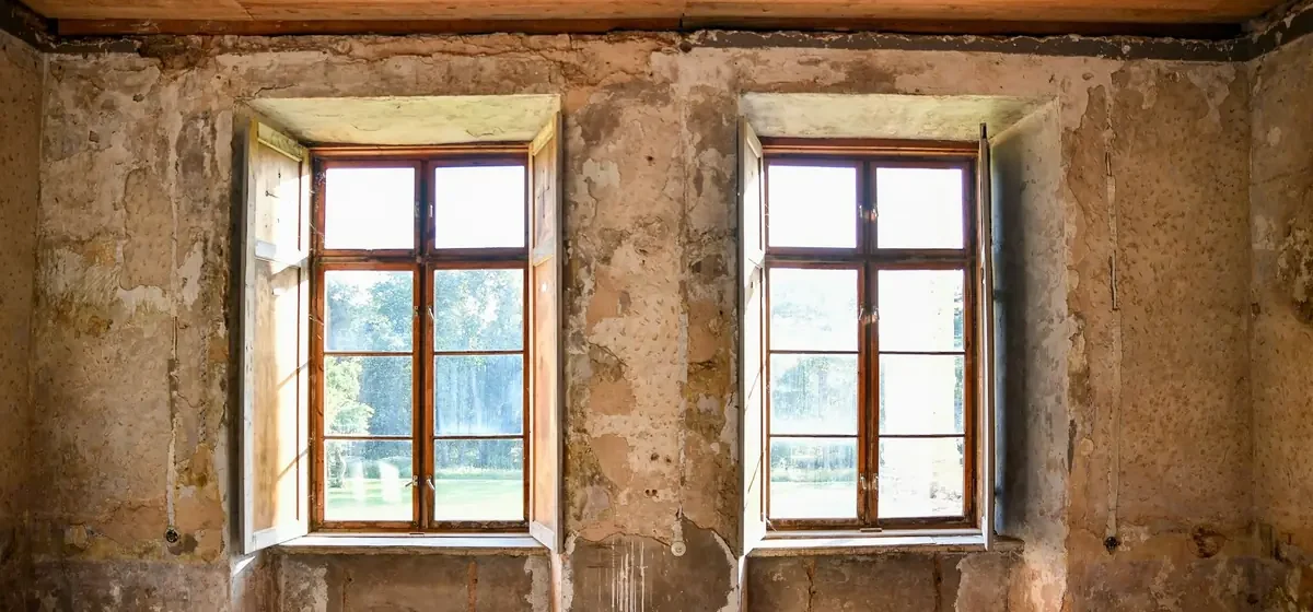Empty old room with two windows and distressed plaster walls