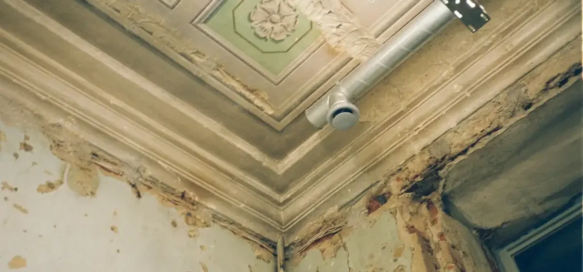 Water-damaged ceiling shedding plaster in a run-down room