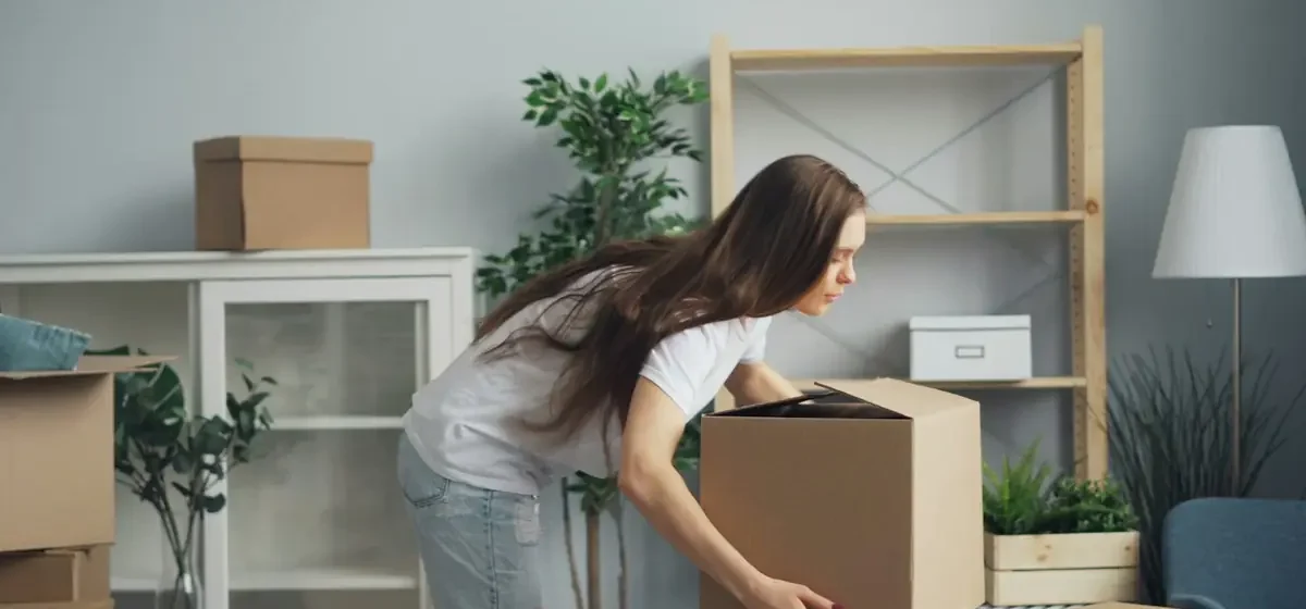 Woman carrying a cardboard box across a living room