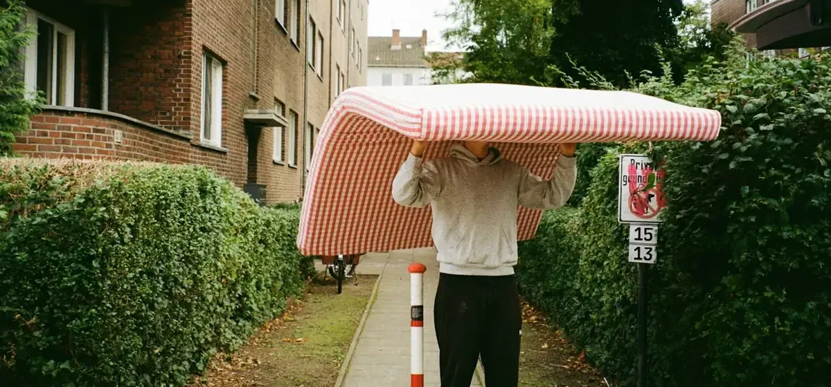 Man carrying a mattress along a residential pavement