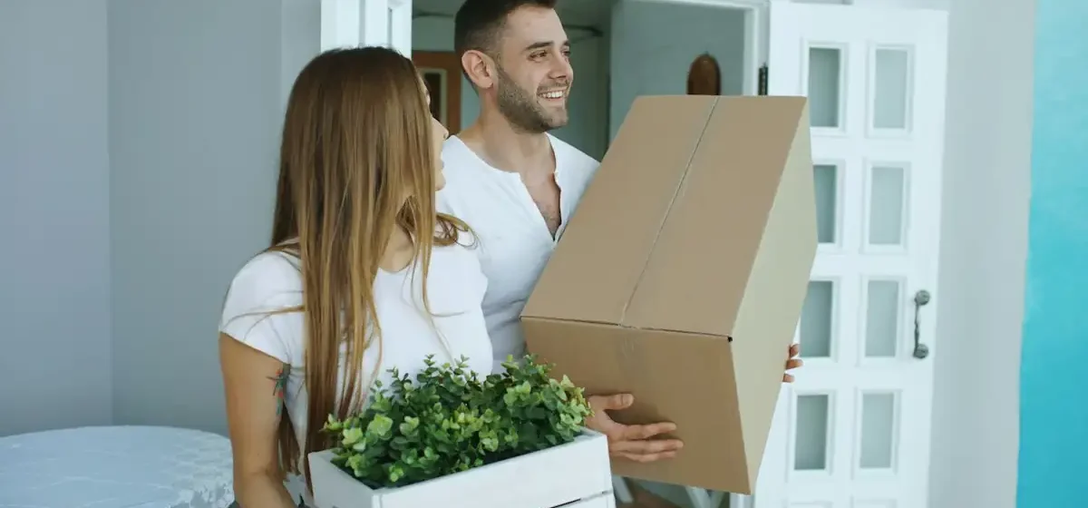 Couple carrying a box and plant through a doorway