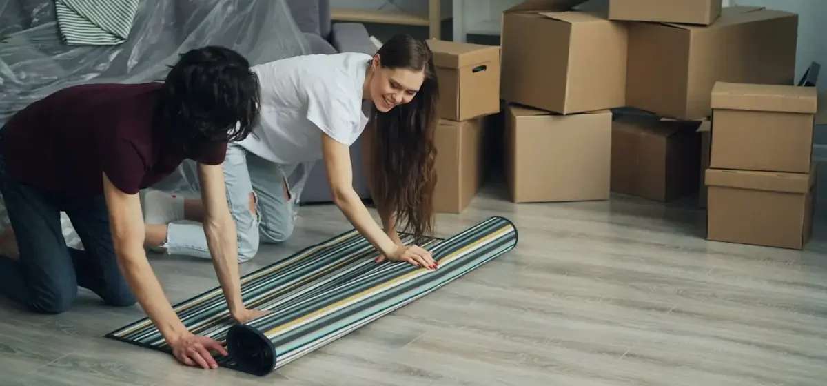 Couple unrolling a rug beside stacked cardboard boxes
