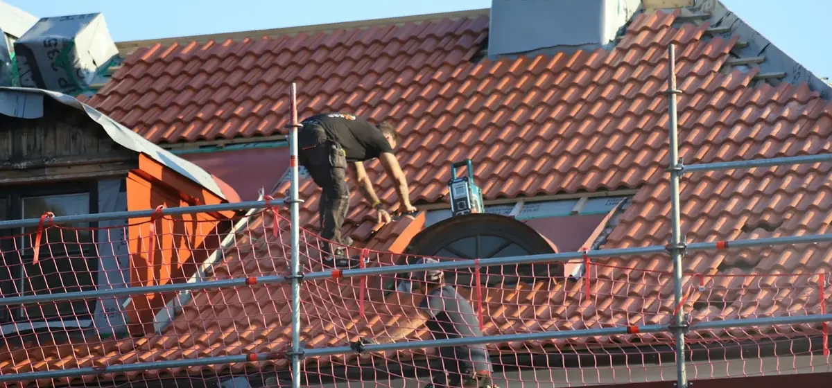 Workman kneeling on a house roof during repair work