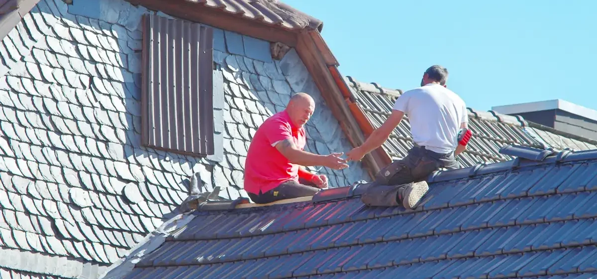 Two roofers sitting on a tiled house roof