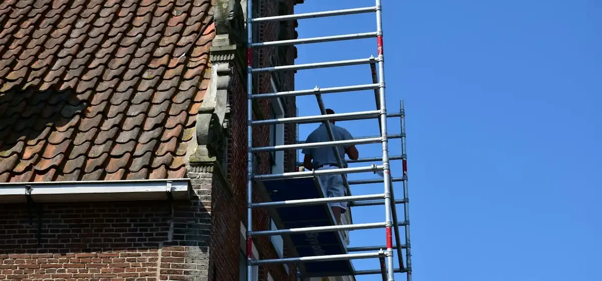 Worker on scaffolding beside a pantiled roof and brick gable
