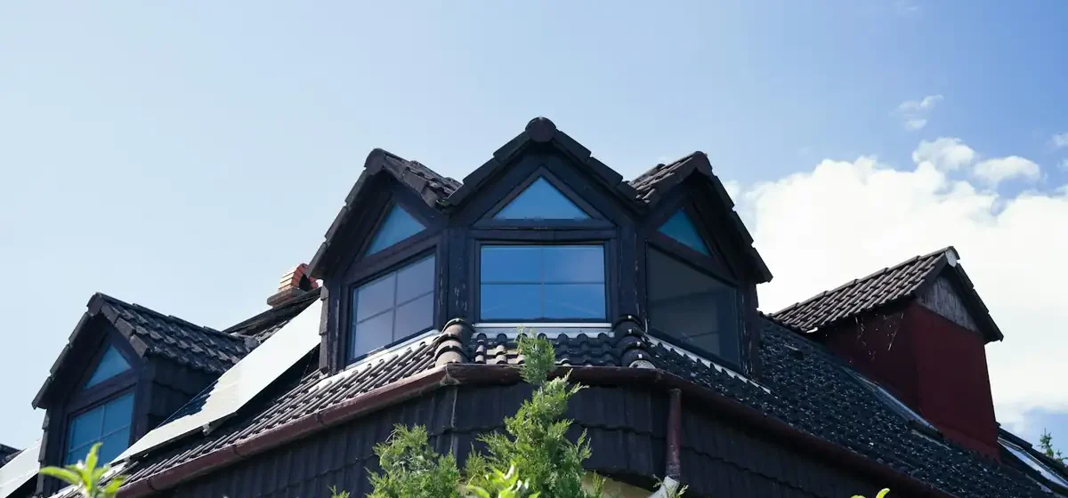 Dark tiled roof with three dormer windows against blue sky